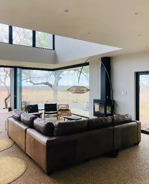Contemporary living room with full-height aluminium glass walls overlooking natural scenery.